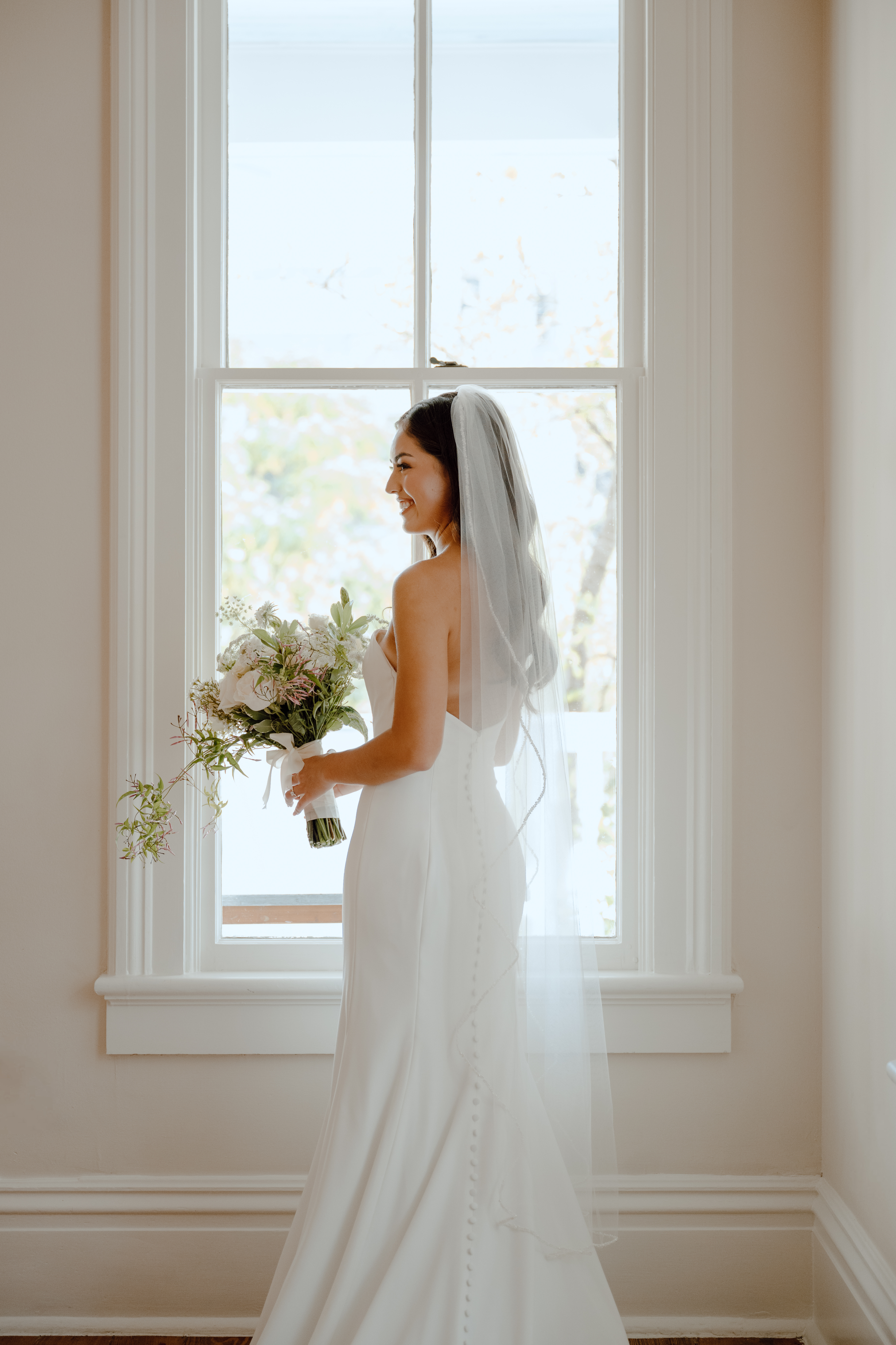 bridal portrait at the Allan house in downtown Austin Texas of bride smiling with long veil and train holding bouquet