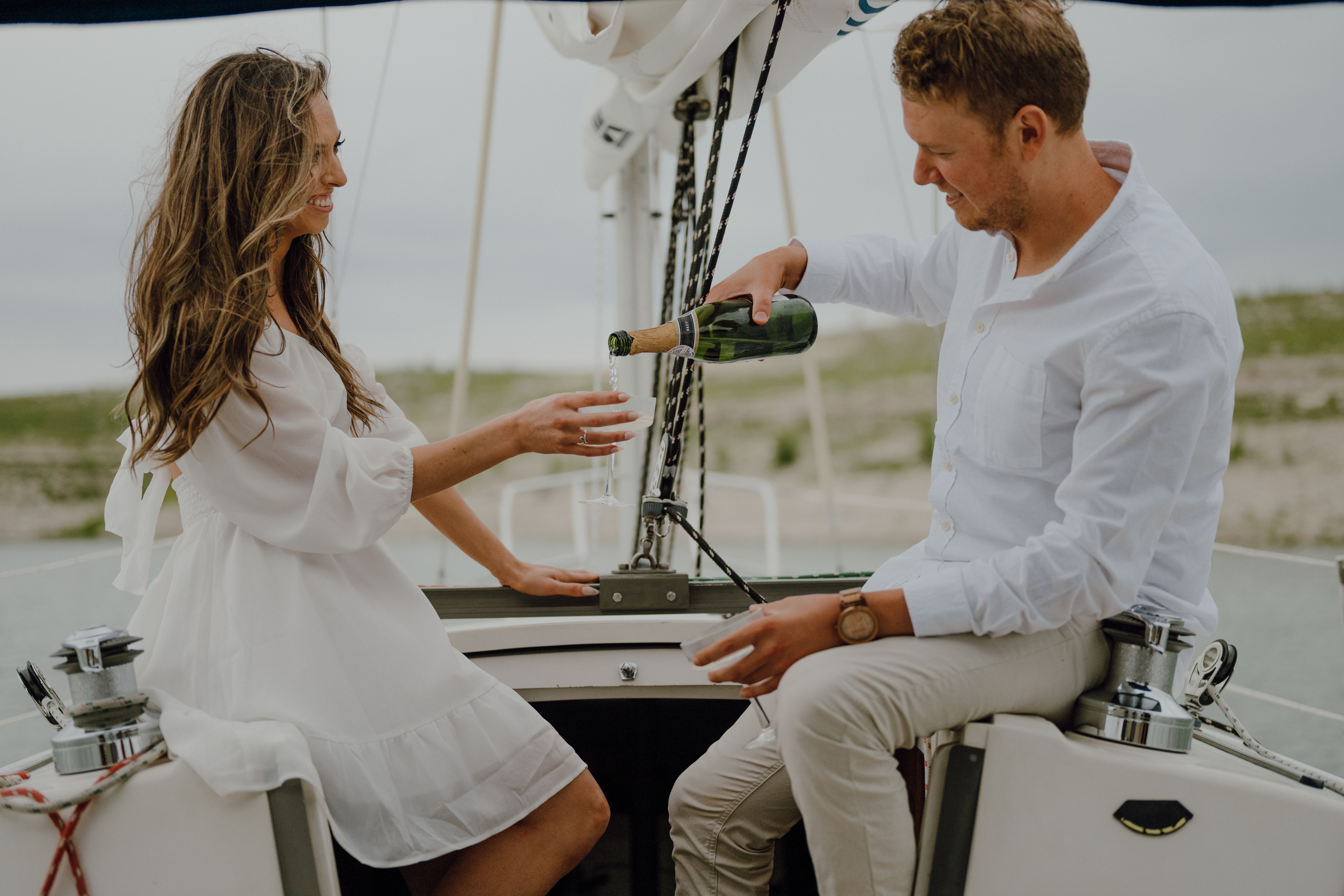 couple pour champagne on a sailboat for their engagement ph